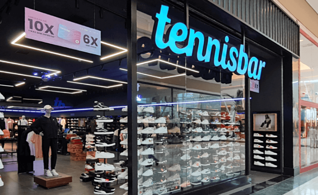 Projeto de arquitetura comercial da loja Tennisbar com fachada de vidro, letreiro luminoso com iluminação LED integrada e exposição estratégica de tênis nas vitrines. Design que maximiza a visibilidade dos produtos e atrai fluxo de clientes.