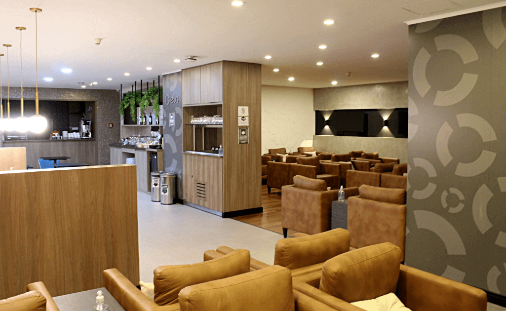 Projeto de arquitetura empresarial para sala VIP Advantage com poltronas em couro caramelo, balcão de selfservice em madeira, iluminação embutida e elementos gráficos institucionais ELO. Espaço que integra conforto, funcionalidade e identidade da marca.